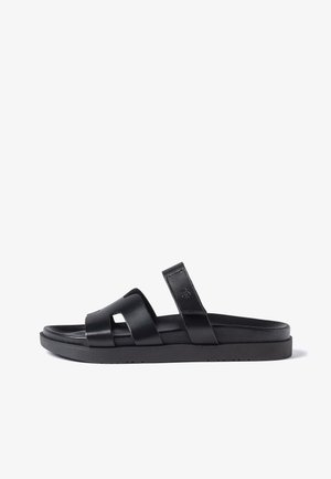 Zwarte open teen instapper met twee brede leren bandjes over de voet en een gevoerd zooltje, gefotografeerd op een witte achtergrond.