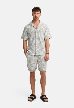 Camisa de manga corta, con cuello, de color gris claro y pantalones cortos a juego con un patrón texturizado; llevados con sandalias oscuras. Atuendo casual de verano.
