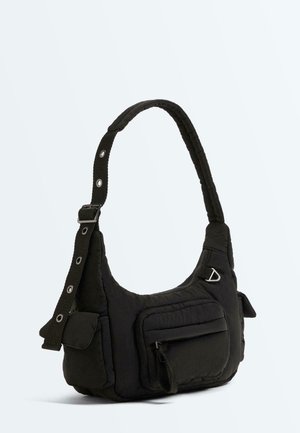 Black padded shoulder bag with adjustable strap, zippered main compartment, front zip pocket, side flap pockets, and metal ring detail.