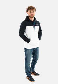 Felpa con cappuccio, pannello anteriore bianco e maniche blu scuro, dotata di tasca kangaroo e lacci blu. Abbinata a jeans blu e scarpe nere.