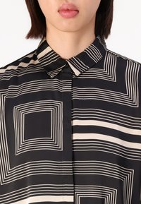 Black and beige button-up shirt featuring a geometric striped pattern with a structured collar and smooth fabric texture.