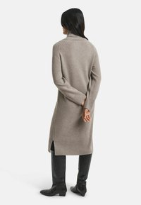 Langes, hellbraunes Strickkleid mit einem Rollkragen, gerippten Akzenten, seitlichen Schlitzen und langen Ärmeln, kombiniert mit hohen, schwarzen, strukturierten Lederstiefeln.