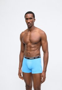 Αθλητικός άνδρας στέκεται φορώντας ανοιχτό μπλε εσώρουχα τύπου boxer της Nike με μαύρη μέση, πάνω σε λευκό φόντο.