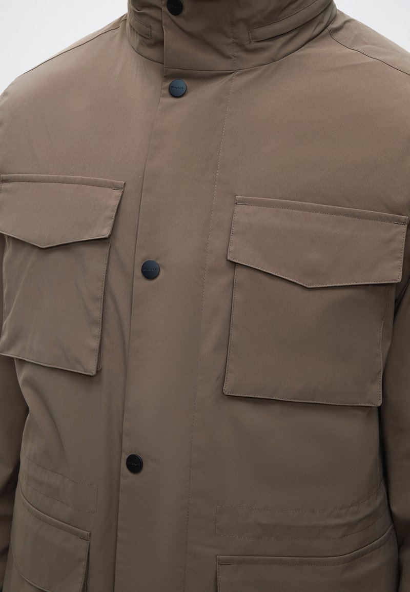 Brown jacket with two large flap pockets on the chest and two black snap buttons down the front.
