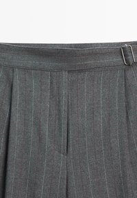 Pantaloni grigi su misura con piega sul davanti, sottili righe verticali in grigio chiaro e bordeaux, e fibbia rettangolare in metallo.