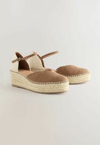 Scarpe con tacco in suede marrone con tomaia beige intrecciata, dotate di cinturino alla caviglia e suole rivestite in juta. Design con punta arrotondata.