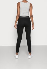Czarne legginsy o gładkiej fakturze, wysokim staniku i dopasowanym kroju, połączone z szarym topem na ramiączkach i białymi trampkami.