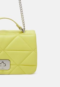 Kultasiininen keltainen käsilaukku, jossa on sileä pinta, suorakulmainen muoto, hopeiset koristelut ja ketjuhihna, joka sisältää etuosan lukitusyksityiskohdan.