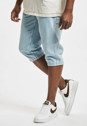 Lys blå denim capri shorts med opfoldet kant og detaljer ved sidesømmen, båret med hvide sneakers med sorte og gyldne accenter.