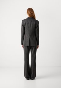 Costume ajusté gris foncé composé d'une veste cintrée et d'un pantalon à jambes larges, tissu texturé avec un motif subtil, lignes épurées et sans ornements.