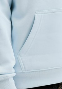 Poche de sweat-shirt bleu clair avec coutures apparentes et tissu côtelé à la taille et aux poignets des manches.