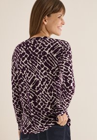 Lange mouw top in paars met een lichte abstracte print. Zacht materiaal, ronde hals, ontspannen pasvorm en zijsplitsingen aan de zoom.