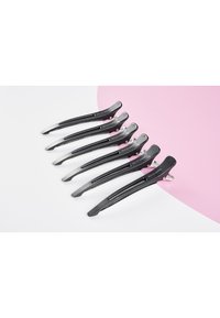 Set med sex svarta hårklämmor med en elegant design, med ett texturerat grepp och släta, metalliska detaljer, arrangerade på en rosa yta.