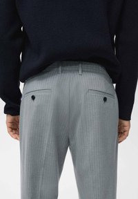 Pantalones grises a rayas con corte entallado, que cuentan con bolsillos traseros con botones. Llevados con un suéter de textura oscura.