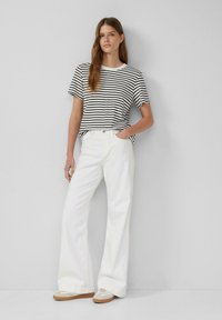 Gestreepte zwart-witte T-shirt met korte mouwen, gecombineerd met witte wijde broek en beige sneakers. Soepele stof, relaxte pasvorm.