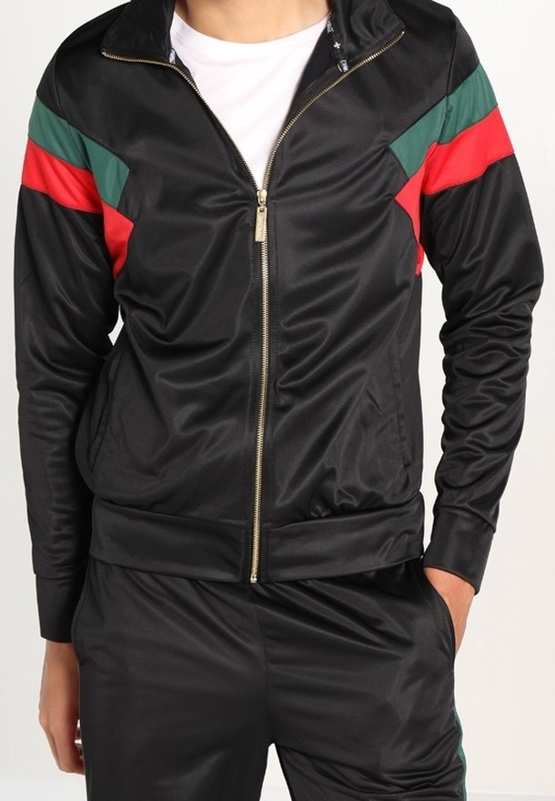 Svart zip-up jacka med gröna och röda accenter på axlarna; tillverkad av slät material; har en guldfärgad dragkedja och ribbad mudd.