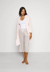 Light pink cardigan with wide sleeves, layered over a white tank top. Striped, mid-calf trousers with a drawstring waist. Barefoot model.