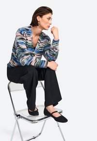Gebreide cardigan met meerkleurige strepen in blauw, roze en groen, voorzien van een diepe V-hals en een enkele knoopsluiting. Zwarte wijde broek en zwarte flats.