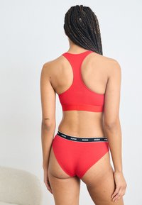 Reggiseno sportivo rosso e slip coordinati realizzati in tessuto morbido, con design a schiena scoperta e una fascia elastica nera con logo sulla biancheria intima.