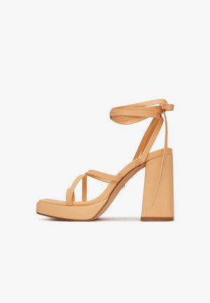 Sandalo con tacco alto beige con cinturini avvolgenti alla caviglia, tacco a blocco, punta aperta e suola con plateau, mostrato di profilo su sfondo bianco.