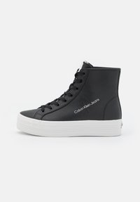 Svarta högskorna är tillverkade av syntetläder med en vit gummisula. Funktioner inkluderar svarta snörningar och "Calvin Klein Jeans"-logotyp på sidan.