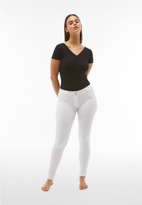 Body nero a maniche corte con scollo a V, abbinato a leggings bianchi aderenti con una finitura liscia e dettaglio in vita con doppio bottone.