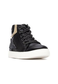 Zapatilla alta de cuero negro con acento de estrella plateada brillante, pestaña en el talón dorada, paneles negros texturizados y cordones negros con patrón sobre una suela blanca.