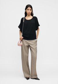 Μαύρο τοπ με κοντά μανίκια και χαλαρή εφαρμογή, σε συνδυασμό με μπεζ παντελόνι ψηλόμεσο και μυτερές μαύρες γόβες. Το μοντέλο κρατά μια τσάντα σε ανοιχτό ροζ χρώμα.