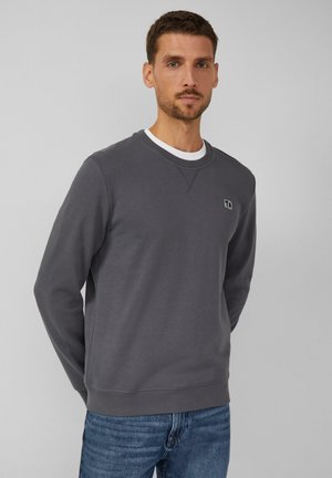 Gray sweatshirt with round neckline and ribbed cuffs. Features a small logo patch on the chest and is made from soft cotton material.