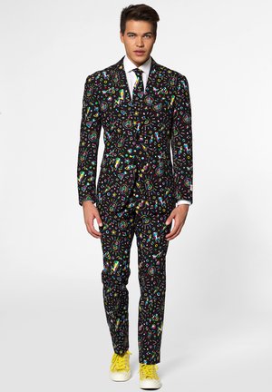 Colorful patterned suit featuring black fabric with vibrant graphics of music symbols, lightning bolts, and geometric shapes; paired with yellow sneakers.