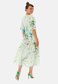 Floral pattern dress in mint green fabric with short sleeves, a tied waist, and a flowing hem, paired with green high-heeled sandals.