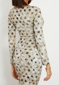 Vestido de manga larga en una mezcla de tonos beige, negro y verde con patrones que presentan diseños circulares abstractos, silueta ajustada y tejido suave.