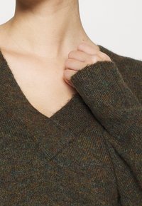 Brunstickad tröja med V-ringning och ribbade muddar, med ett texturerat tyg som har subtila färgfläckar.