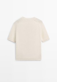 Korte mouws crème gebreide trui met geribde kraag, manchetten en zoom, plat liggend met de achterkant naar boven op een witte achtergrond.