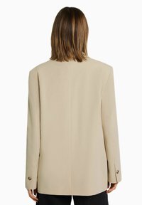 Beige op maat gemaakte blazer met een gestructureerde silhouet, enkele knoopsluiting en lange mouwen met een knoopmanchet. Soepele stoftextuur.