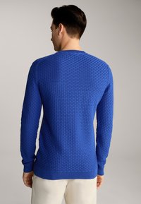 Pull en tricot bleu avec un motif texturé, des manches longues et un ourlet côtelé. Le tissu semble doux avec une légère élasticité.