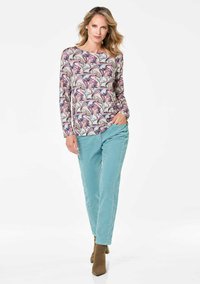 Langarmhemd mit floralem Muster in Lila, Pink und Grün. Kombiniert mit hellblauen Hosen und braunen Stiefeletten.