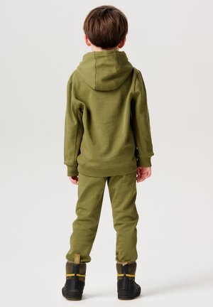Olivgrüner Kapuzenpullover und passende Jogginghose aus weichem Stoff. Verfügt über gerippte Bündchen und eine entspannte Passform. Getragen mit schwarzen Stiefeln.
