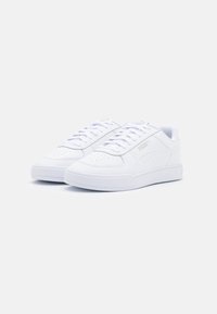 Bílé pohodlné tenisky z hladkého materiálu, s perforovanými detaily, plochými tkaničkami a logem na boku. Minimalistický design.