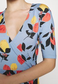 Wickelkleid aus hellblauem Stoff mit floralem Muster und roten, gelben sowie schwarzen Blättern. Kurze Ärmel und ein V-Ausschnitt.