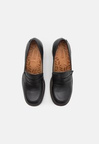 Scarpe slip-on in pelle nera con tomaia liscia, punta arrotondata e dettaglio decorativo sulla tomaia. All'interno presentano una soletta marrone con motivo.