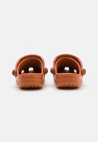 Saboti din cauciuc maro cu spate deschis, talpă texturată și ventilații laterale. Designul prezintă o formă simplă, rotundă și accente cu butoane.