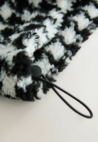 Pătură pufoasă alb-negru cu un model texturat, în carouri. Dispune de un sistem de închidere cu șnur negru și un toggle rotund. Material moale și confortabil.