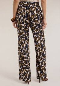 I pantaloni a gamba larga presentano una stampa leopardata astratta audace con colori verde, blu navy e bianco. Visibile anche la cintura elastica e la texture del tessuto morbida.