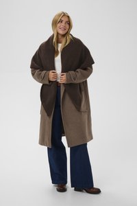 Brązowy długi płaszcz z mieszanki wełny z szerokim kołnierzem w formie szala, bocznymi kieszeniami i zapięciem na guziki. Połączony z granatowymi rozszerzanymi dżinsami i brązowymi botkami na obcasie.