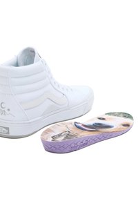 Weißer High-Top-Sneaker mit strukturierten Nähten und Logo, neben einer bunten Innensohle mit dem Gesicht eines Hundes auf einem lila Boden.