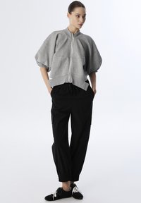 Grijze cropped sweatshirt met een staande kraag en een voorkleur. Gecombineerd met zwarte cargo broeken met elastische boorden en zakken.