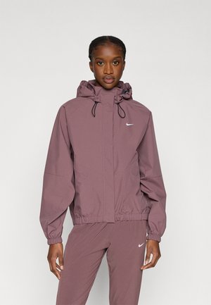 Lilla nylonjakke med hætte, forlommer, elastiske manchetter og snøre i kanten. Har en lille hvid Nike-logo på brystet.