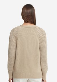 Stickad tröja i ljusbeige med texturerade ärmar. Har en rund halsringning och ribbad mudd. Baksidan har en slät tyg.