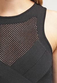 Lähikuva mustasta ilmanhihaisestä paidasta, jossa on verkkoneulekuvio rinnan kohdalla ja kiinteää neulekangasta sivuilla ja olkaimissa.